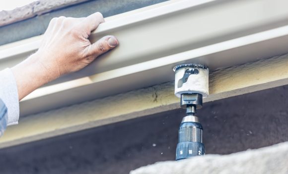 Worker Attaching Aluminum Rain Gutter to Fascia of House.