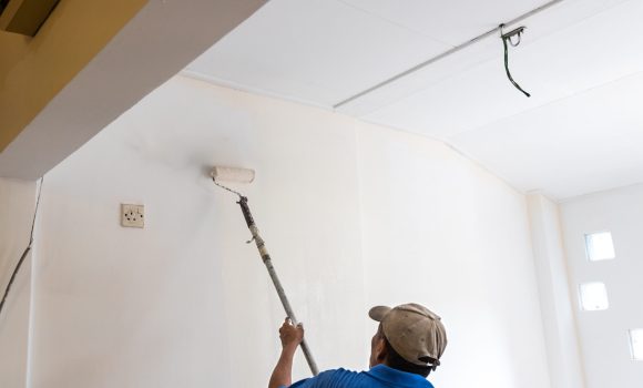 Worker painting wall with new coat of paint using paint roller during renovation project